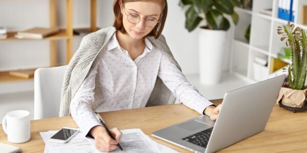 pozyskiwanie klientów księgowość – księgowa pracująca przy dokumentach i laptopie w biurze rachunkowym